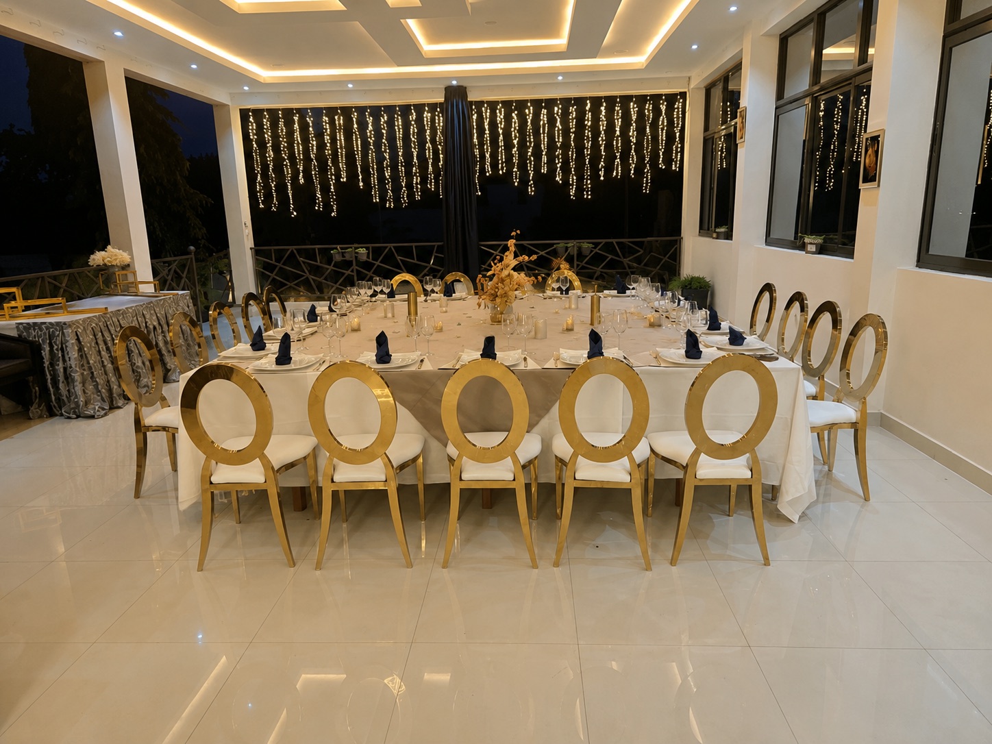 Banquet dressé dans la salle événementielle, chaises dorées et guirlandes lumineuses
