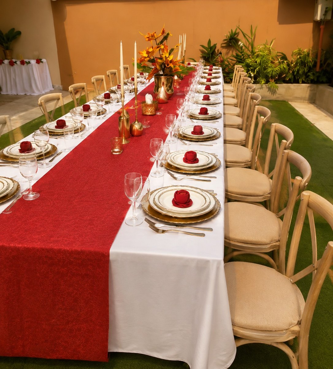 Longue table de mariage dressée au jardin, chemin de table rouge, roses et chandeliers dorés