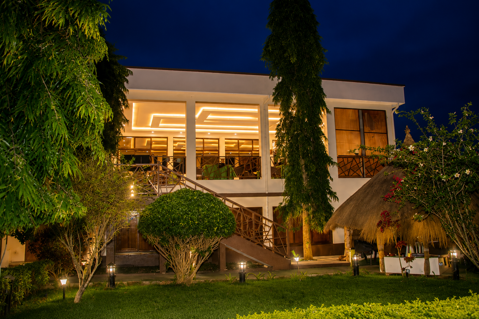 Vue nocturne de HappyLand Prestige : escalier illuminé, jardin verdoyant et restaurant panoramique